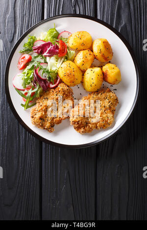 Crispy steaks in sesame breading with new potatoes and fresh salad close-up on a plate on the table. Vertical top view from above Stock Photo