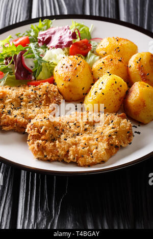 Pork cutlet in sesame breading with new potatoes and fresh salad close-up on a plate on the table. vertical Stock Photo