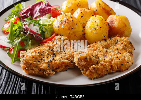 Delicious fried steaks in sesame breading served with new potatoes and fresh salad close-up on a plate on the table. horizontal Stock Photo