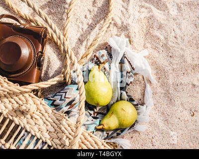 Wicker basket, vintage camera and shawl on sand background. Top view, close-up Stock Photo