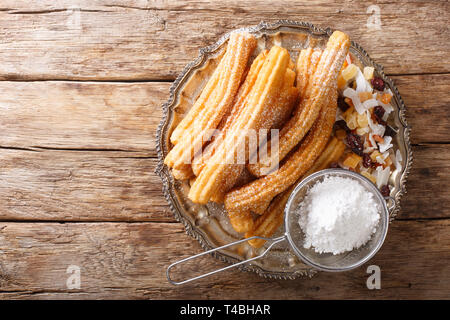Freshly made hot churros with powdered sugar and candied fruits close-up on the table. horizontal top view from above Stock Photo