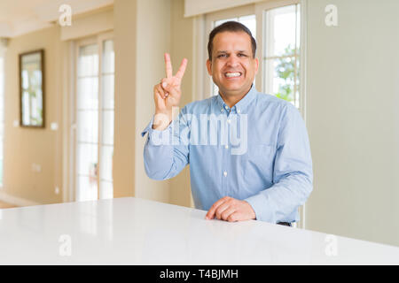 Middle age man sitting at home showing and pointing up with fingers number two while smiling confident and happy. Stock Photo