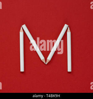 The letter 'M' made from grad-white pencils on a plain red background Stock Photo