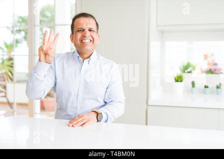 Middle age man sitting at home showing and pointing up with fingers number three while smiling confident and happy. Stock Photo