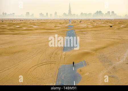 View from above, stunning aerial view of an unidentified person walking on a deserted road covered by sand dunes in the middle of the Dubai desert.