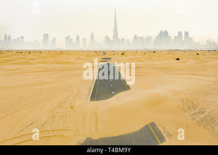 Stunning aerial view of an unidentified person walking on a deserted road covered by sand dunes in Dubai desert. Dubai skyline surrounded by fog.