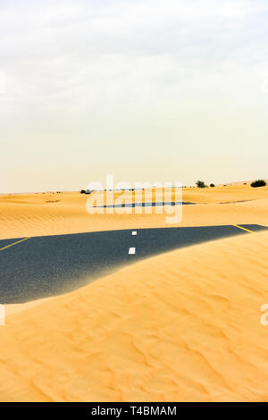 (Selective focus) Stunning view of a deserted road covered by sand dunes. Empty road that run through the Dubai desert during sunset. Dubai. Stock Photo