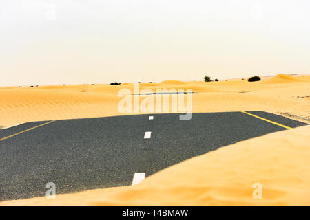 (Selective focus) Stunning view of a deserted road covered by sand dunes. Empty road that run through the Dubai desert during sunset. Dubai. Stock Photo