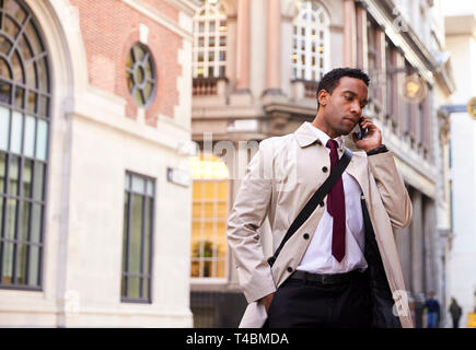 Millennial black businessman standing on a street in London talking on his phone, low angle Stock Photo