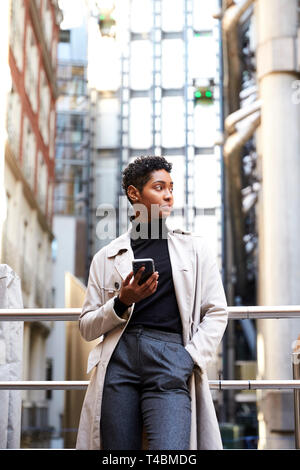 Fashionable young black woman leaning on handrail in the city area holding smartphone, low angle, close up, vertical Stock Photo