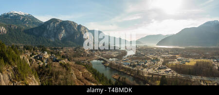 Aerial panoramic view of a small town with Chief Mountain in the background during a sunny day. Taken in Squamish, North of Vancouver, British Columbi Stock Photo