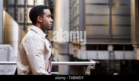 Waist up side view of young black businessman walking past modern architecture in there city, London UK