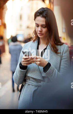 Young white businesswoman standing on a busy London street using smartphone, close up, vertical Stock Photo