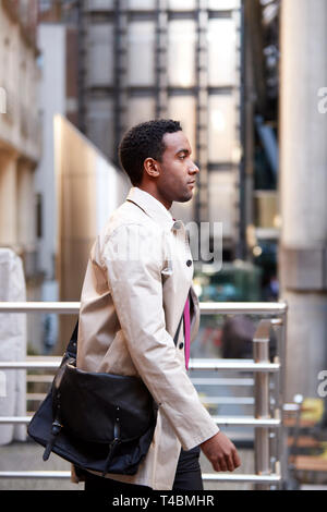 Side view of a young black businessman walking in a street in the city, London UK, close up