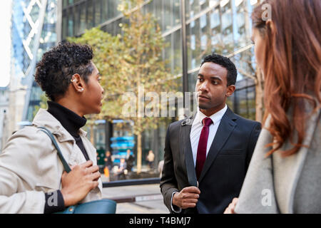 Three millennial business colleagues standing on the street talking, low angle, close up Stock Photo