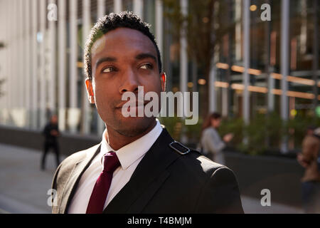 Young black businessman wearing black suit standing on the street smiling, looking away, close up Stock Photo