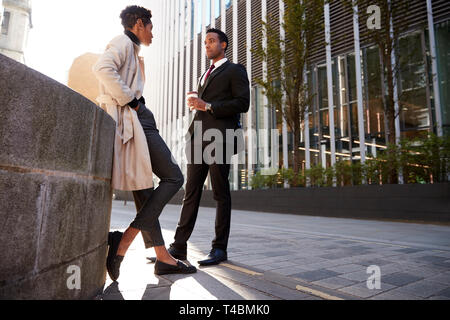 Two young adult colleagues standing on the street talking, low angle Stock Photo