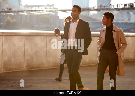 Two business colleagues walking by the Thames riverside in the city of London talking, man holding takeaway coffee Stock Photo