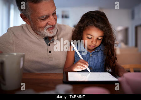 Senior Hispanic man with his young granddaughter using stylus and tablet computer, front, close up Stock Photo