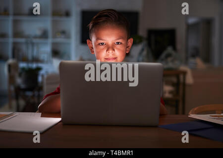 Pre-teen Hispanic boy sitting at dining table doing his homework using a laptop computer, close up Stock Photo