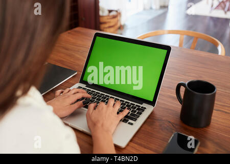 Over shoulder view of woman sitting at table using laptop computer at home, close up Stock Photo