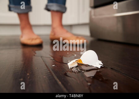 A broken egg on the kitchen floor after a small cooking accident, feet in the background, low angle Stock Photo