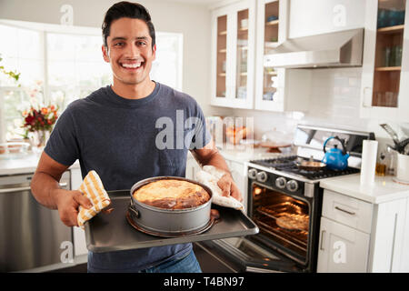 Smiling millennial Hispanic man standing in kitchen presenting the cake he has baked to camera Stock Photo