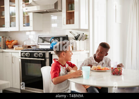 Two pre-teen male friends sit talking in the kitchen during a playdate at one boy’s house Stock Photo
