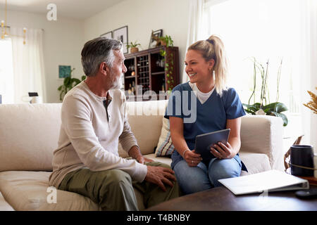 Female healthcare worker using a tablet computer with a senior Hispanic man during a home visit Stock Photo