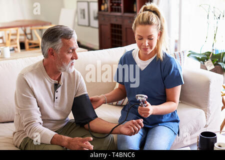 Female healthcare worker making home visit to a senior man taking blood pressure Stock Photo