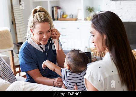 Female healthcare worker visiting young mum and her infant son at home, using stethoscope, close up Stock Photo