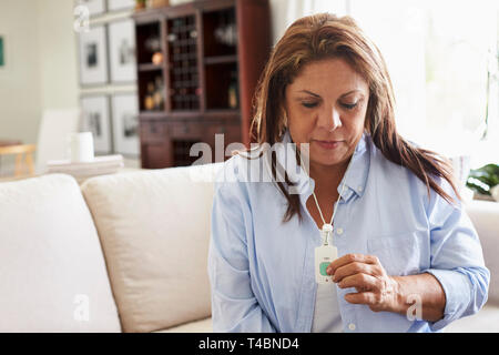 Middle aged Hispanic woman at home, pushing an assistance alarm which she is wearing around her neck Stock Photo
