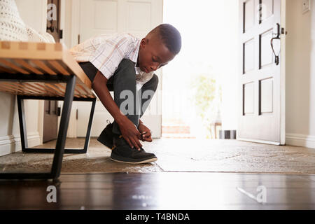Low angle view pre-teen black boy tying his shoes before leaving home, selective focus Stock Photo