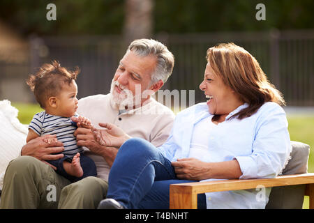 Senior couple sitting in the garden with their baby grandson, smiling at him, front view Stock Photo