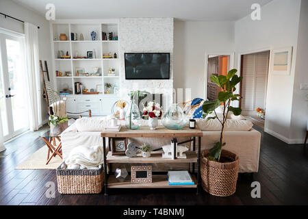 A family living room with white walls and dark wood floorboards seen in daylight, from behind the sofa, which sits in a central position, no people in shot Stock Photo