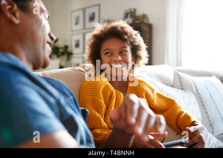 Close up of father and daughter sitting on sofa in the living room looking at each other and laughing, selective focus
