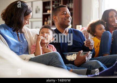 Three generation family family sitting on the sofa in living room, watching TV and eating popcorn, selective focus Stock Photo