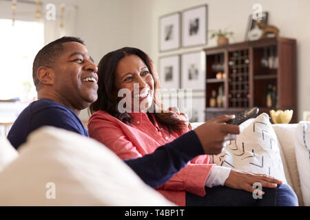 Close up of middle aged couple sitting on the sofa in their living room using remote and watching TV, laughing, close up Stock Photo