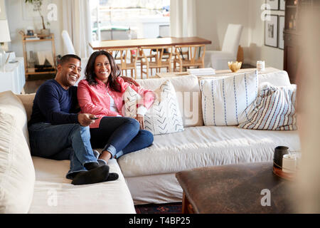 Middle aged couple reclining on the sofa in their living room watching TV, selective focus Stock Photo