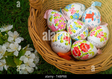 Close up of colorful decorted hand painted Easter eggs in a basket on grass with cherry bossom Stock Photo