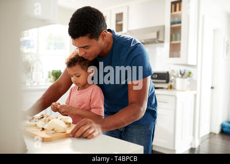 Millennial man standing at kitchen worktop preparing food with his toddler son, close up, selective focus