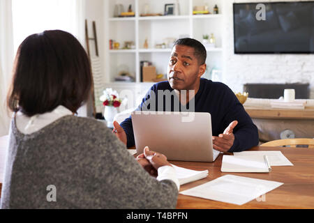 Millennial man with laptop computer giving financial advice to a woman sitting at the table in her dining room, selective focus Stock Photo