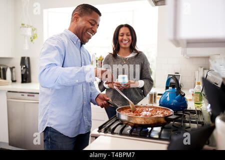Millennial Hispanic man standing in the kitchen cooking with his partner standing beside him, backlit Stock Photo