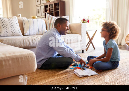 Side view of grandad and granddaughter sitting opposite each other cross legged on the floor in the living room constructing a model robot together, close up Stock Photo