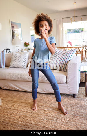 Pre-teen black girl dancing and singing in the living room at home using her phone as a microphone, full length, vertical