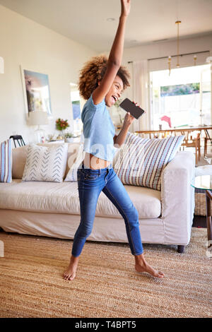 Pre-teen black girl dancing and singing in the living room at home using her phone as a microphone, side view, full length, vertical