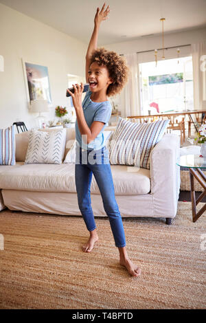 Pre-teen girl dancing and singing in the living room at home using her phone as a microphone, full length, vertical