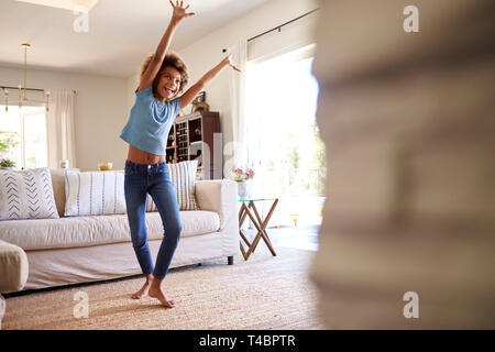 Pre-teen girl dancing and singing along to music on TV in the living room at home, three quarter length