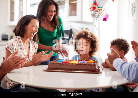 Pre teen girl blowing out the candles on birthday cake sitting at table in the kitchen with her three generation family, selective focus Stock Photo