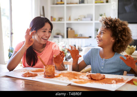 Two girlfriends having fun playing with modelling clay at home, laughing and showing their dirty hands to each other, close up Stock Photo